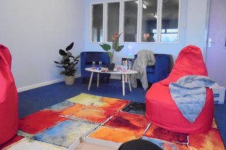 An education department with bright red bean bags, multi-coloured rug,  table and blue chairs